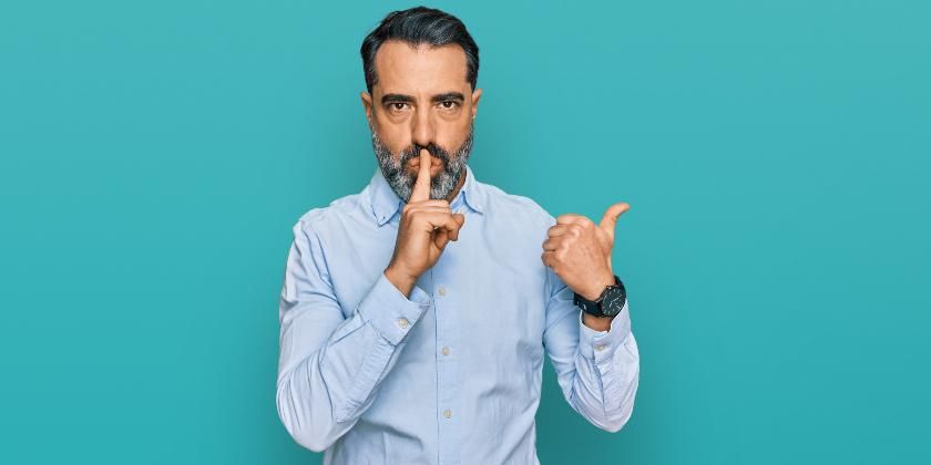 Man in blue shirt putting finger to his mouth