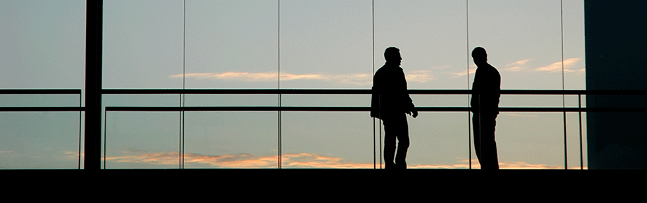 silhouettes of two men standing and watching sunset