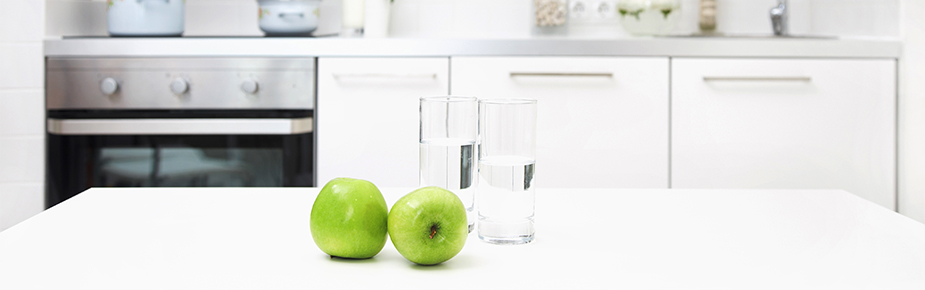 two green apples and glasses of water sitting on a kitchen bunker