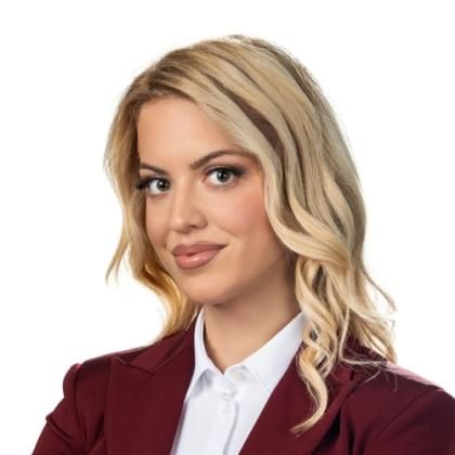 Portrait of Teodora Vujosevic, blond curly hair till the shoulder,  wearing a white shirt and a dark red blazer-