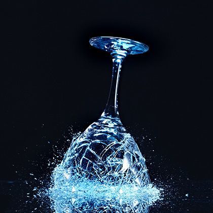 blue wineglass shattering on reflecting ground 的照片