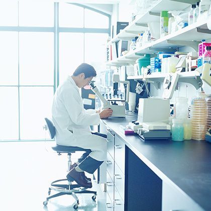 side view of scientist looking into microscope in bright research lab