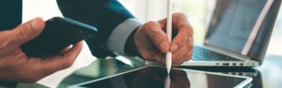 businessman writing on a tablet whilst holding a mobile phone in the other hand