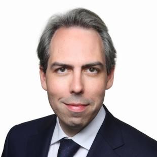 Portrait professionnel de David Guitton, en costume sombre et chemise blanche avec cravate, photographié de face sur fond blanc.