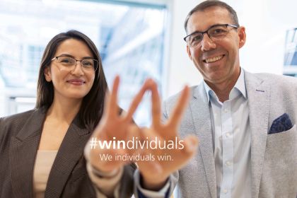 Zwei Personen, eine Frau und ein Mann im Büro von CMS  Wien, stellen gemeinsam das Viktory-Zeichen, zusammengeführt zu einem W, dar, um unser angeführtes Arbeitgeberversprechen "#windividuals - We individuals win." visuell zu unterstreichen.