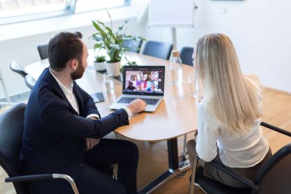 Zwei Personen, ein Mann und eine Frau, halten ein Teammeeting  im CMS Büro in Wien und führen ein Gespräch an einem runden Tisch mit Laptop