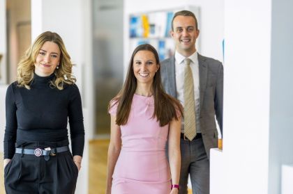 Three business professionals standing together in an office hallway, engaged in conversation.